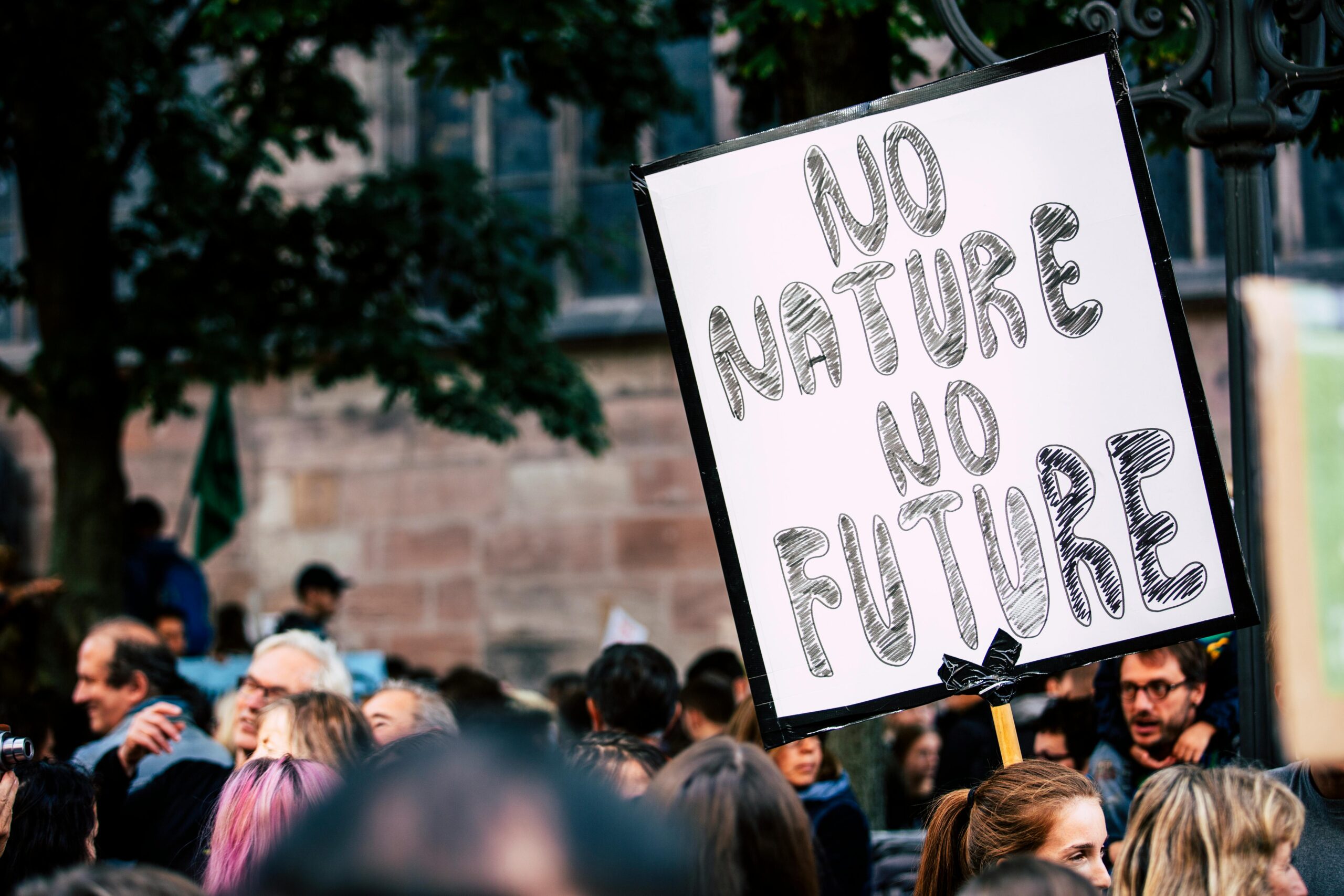 Large group of people rallying with a sign advocating for nature protection and climate action.